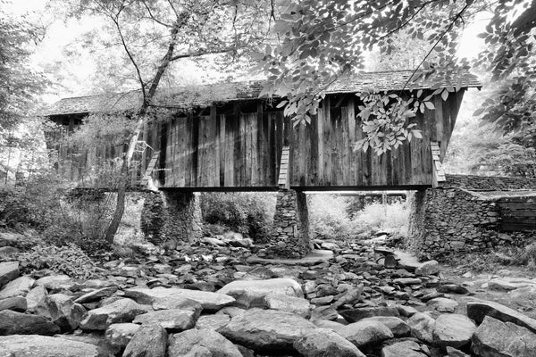Black and white photograph of the historic Pisgah Covered Bridge built along a rural road through the forest in North Carolina in 1911 at a cost of $40.