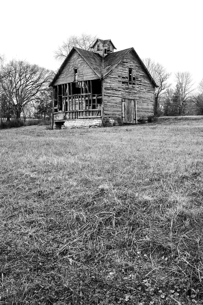 Black and white photograph of a historic abandoned barn in the middle of a rural field.