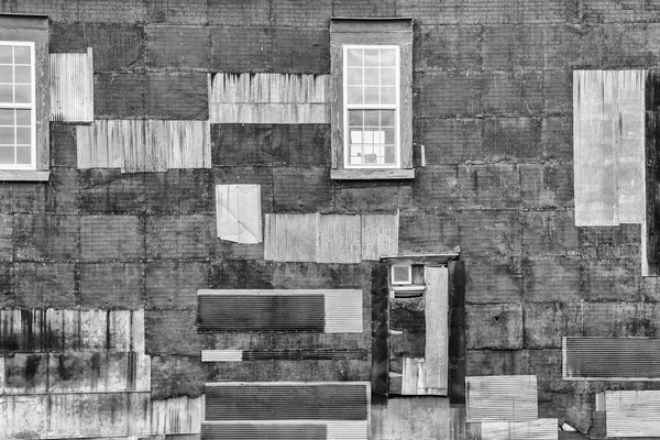 Black and white photograph of a patchwork wall of rusty corrugated metal and doors and windows. The structure is an old cotton warehouse that now discreetly houses the main design workshop of Auburn University's Rural Studio in Newbern, Alabama.