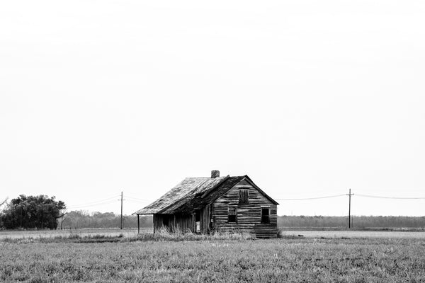 Black and white landscape photograph with an abandoned old wooden shack amidst rural farm fields.