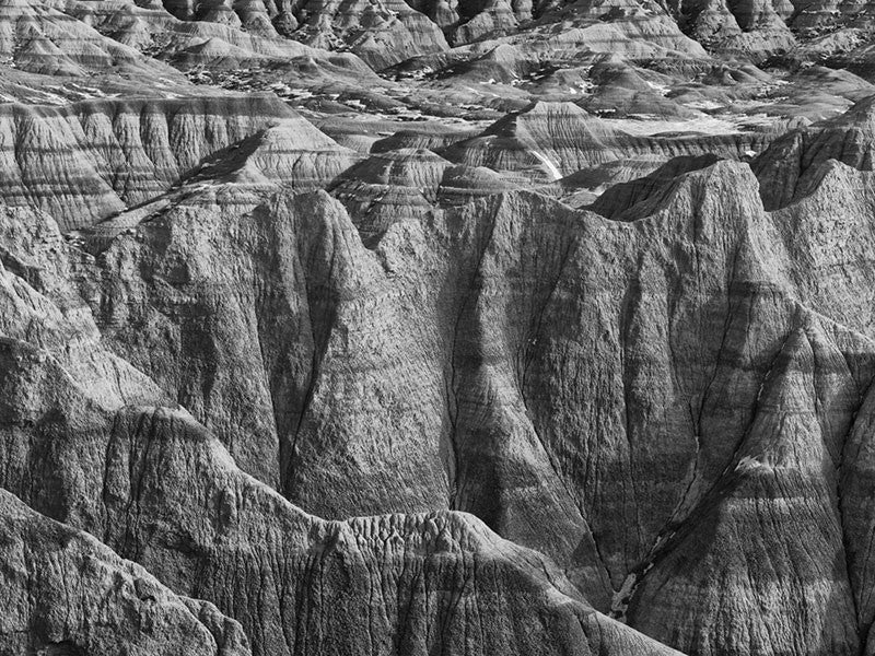 Black and white landscape photograph of the rugged, wrinkled and treeless terrain at the Badlands of South Dakota.