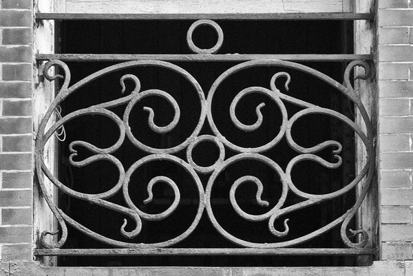 Black and white architectural detail photograph of a New Orleans window with a decorative ironwork screen.