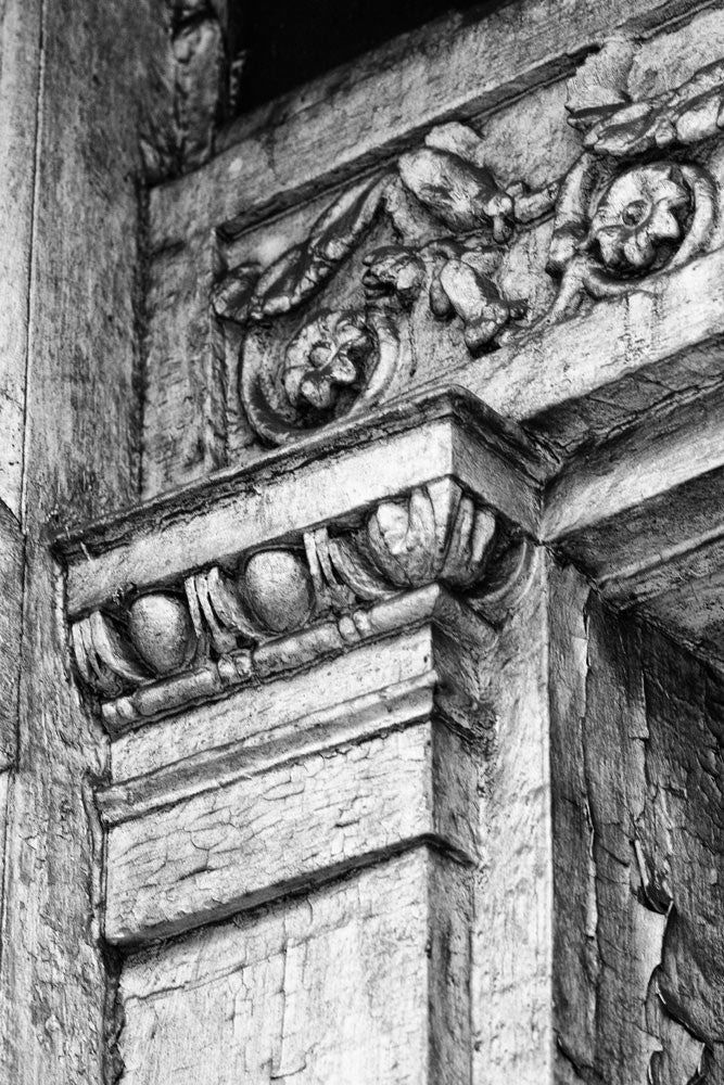 Black and white architectural detail photograph of beautifully decorative but rotting woodwork in the front porch of an abandoned house in New Orleans.