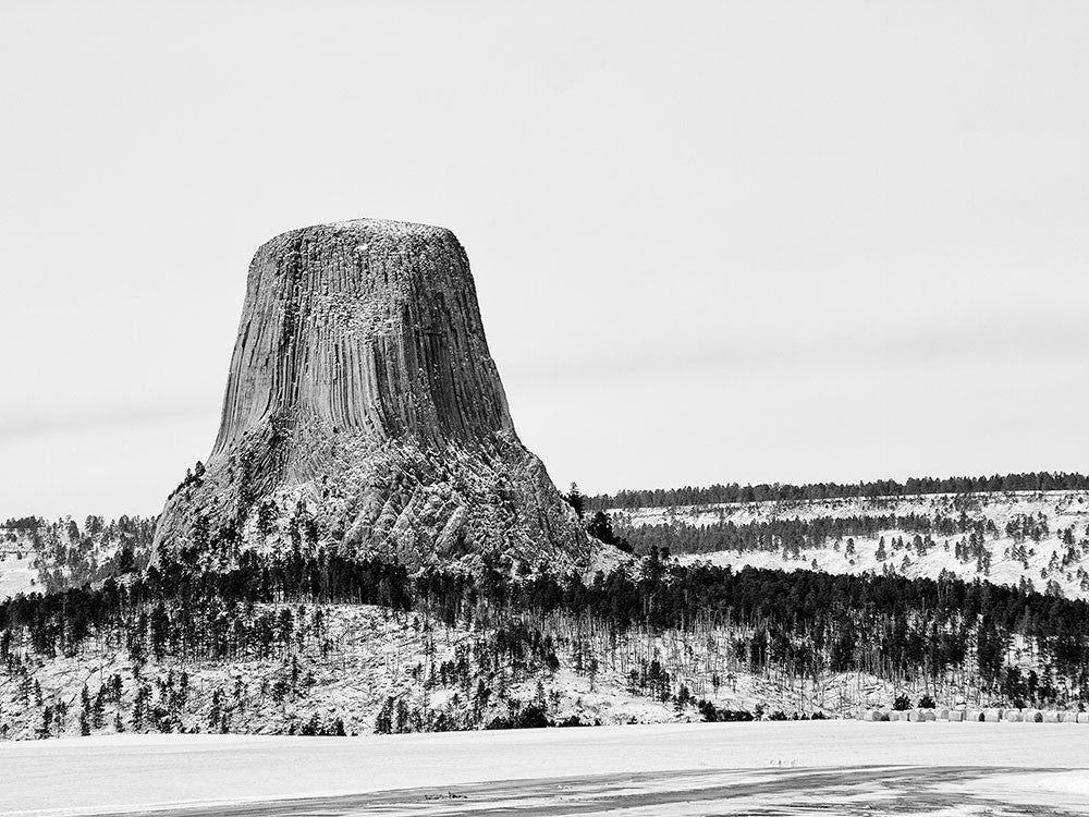 Black and white landscape photograph of Devil's Tower, Wyoming, seen in winter with light snow on the ground.