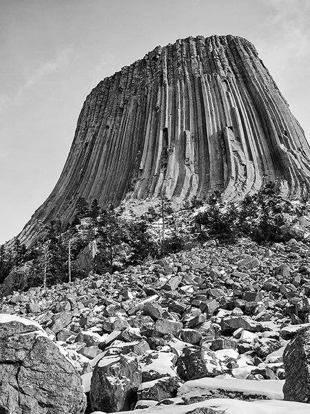 Black and white landscape photograph of Devil's Tower, Wyoming, seen from below where stone rubble has collected near the base.