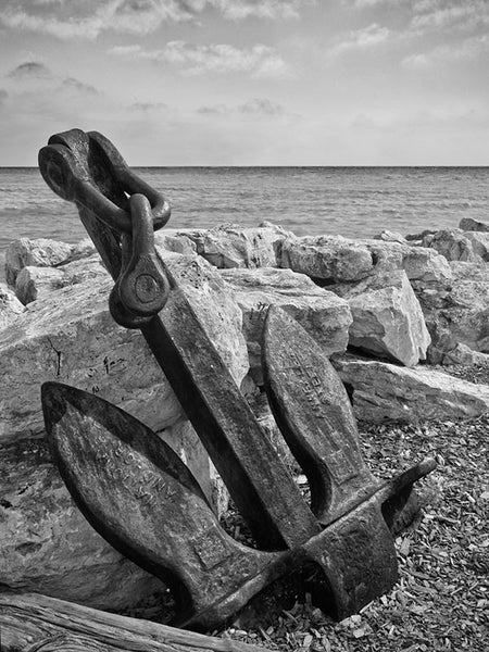 Black and white photograph of a ship's anchor perched against rocks on the shore of Lake Michigan in Wisconsin.