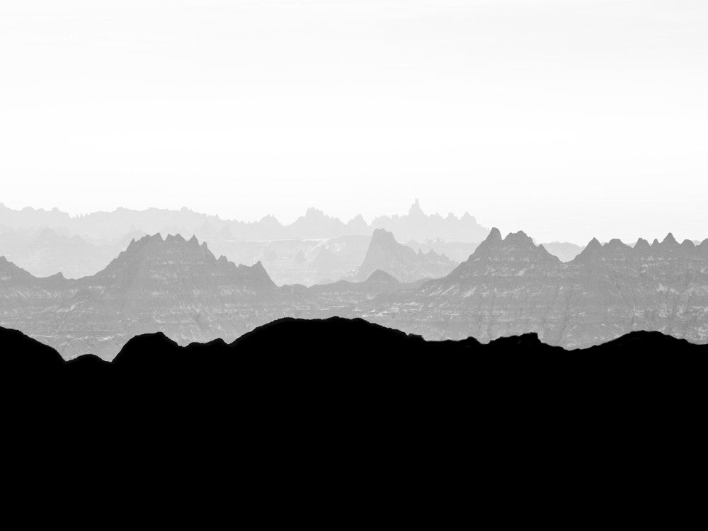 Black and white landscape photograph of misty peaks in early morning light at the Badlands of South Dakota.