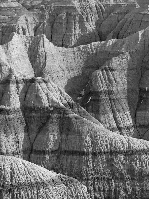 Black and white landscape photograph of the rugged, wrinkled, and treeless terrain at the Badlands of South Dakota.