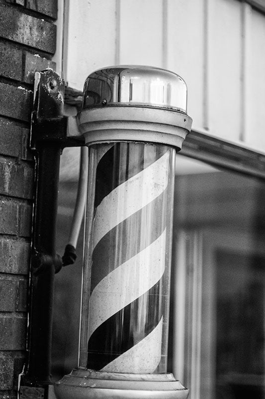 Black and white photograph of a barber pole outside an old-fashioned southern barber shop in downtown Murfreesboro, Tennessee.