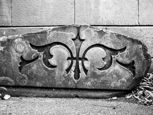Black and white landscape photograph of a broken architectural fragment with a carved design sitting in a parking lot