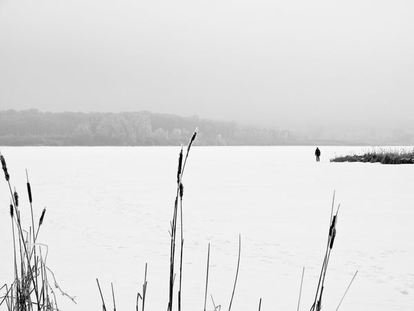 Black and white photograph of a white winter landscape featuring a dark figure walking across a frozen lake in Madison, Wisconsin.