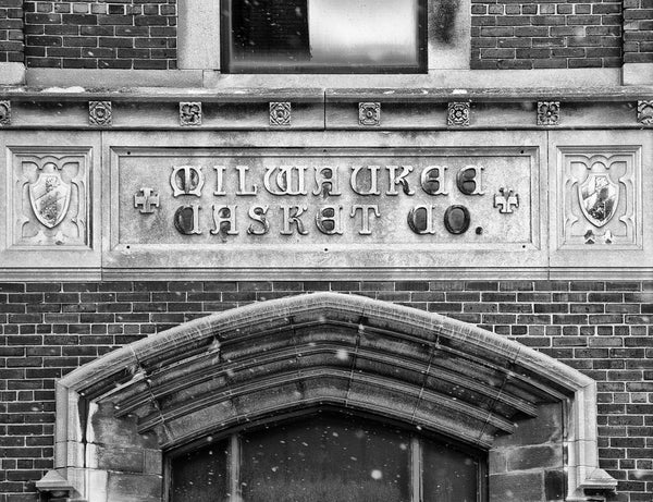 Black and white photograph of the sign on the old Milwaukee Casket Co. building in downtown Milwaukee. This Neogothic Revival building was constructed in 1929 at 1418 West St. Paul Avenue in Milwaukee. The location served as a shipping operation for Milwaukee Casket Company, and was later an air conditioning/heating repair service.