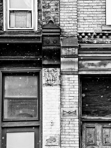 Black and white architectural detail photograph of the seam where two old buildings in old Milwaukee meet, with snow flying in the air.