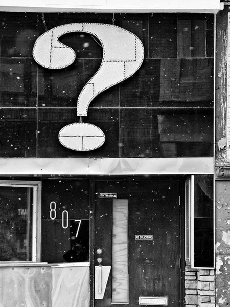 Black and white architectural photograph of a storefront in Milwaukee with a huge question mark above the door, and snow flurries blowing in the air.