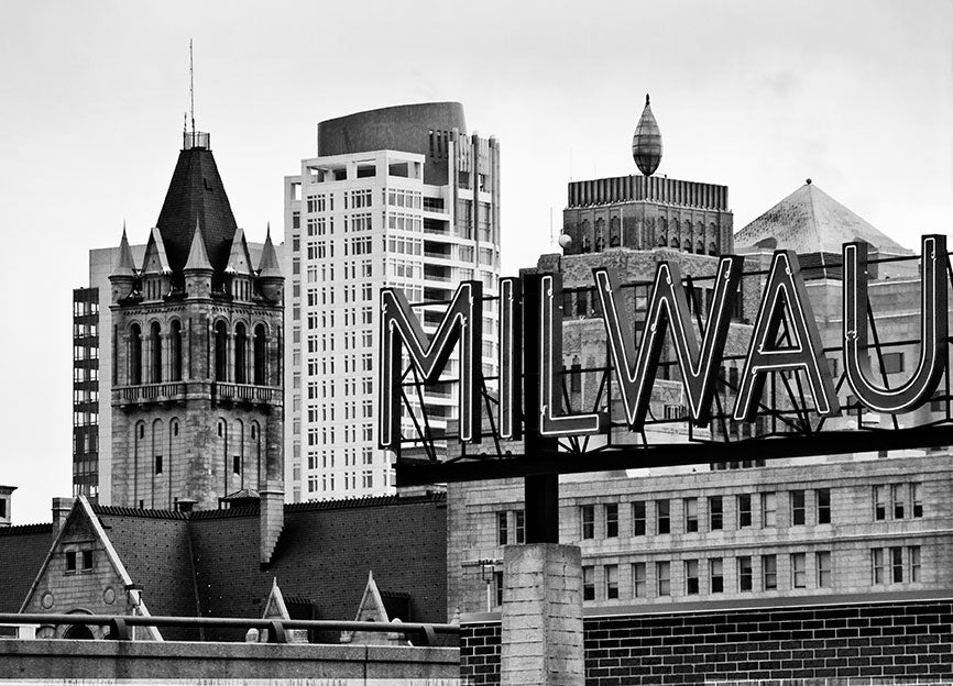 Black and white photograph of the Milwaukee skyline with the "Milwaukee" sign from the Milwaukee Public Market in the foreground.