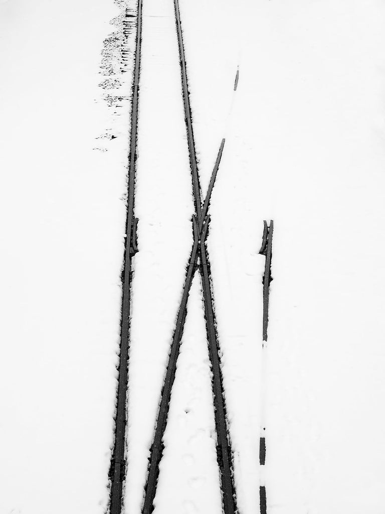 Black and white photograph of railroad tracks seen from above, partially covered in snow.