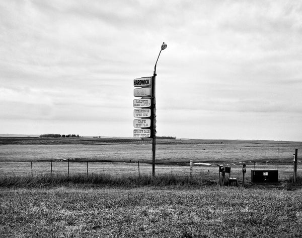 Black and white landscape photograph of Minnesota prairie in early Spring, with a vintage sign in the center of the frame.