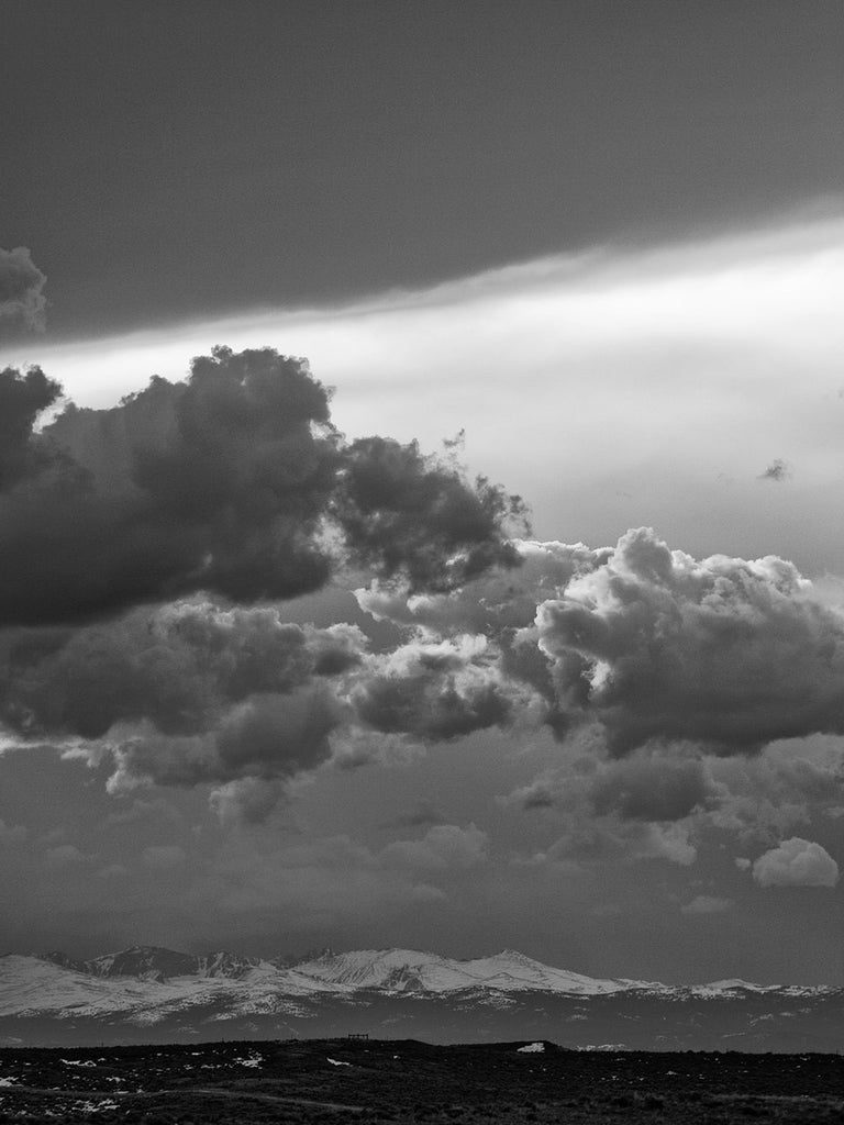 Black and white landscape photograph of turbulent storm clouds over the snowy mountains of Eastern Wyoming.