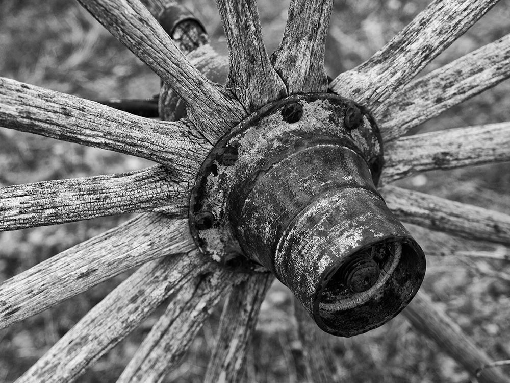 Black and white photograph of a weathered antique wagon wheel on an abandoned buckboard wagon in the wilderness of Wyoming.