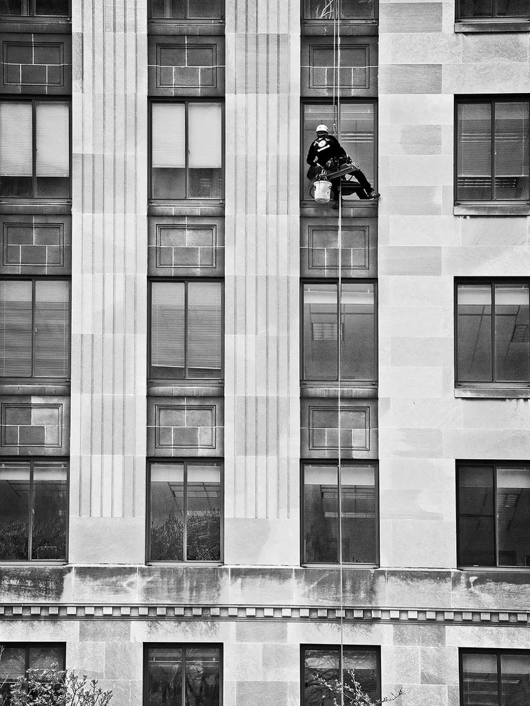Black and white photograph of a guy washing office windows outside a high-rise building on the Capitol Square in downtown Madison, Wisconsin. 
