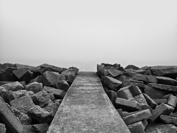 Black and white landscape photograph of a sidewalk that seems to end at nothingness, with just a little bit of Lake Michigan visible in dense fog.