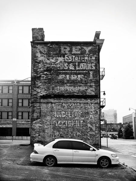 Black and white photograph of a narrow old building in Racine, Wisconsin, featuring layers of fading wall ads on its brick exterior wall.