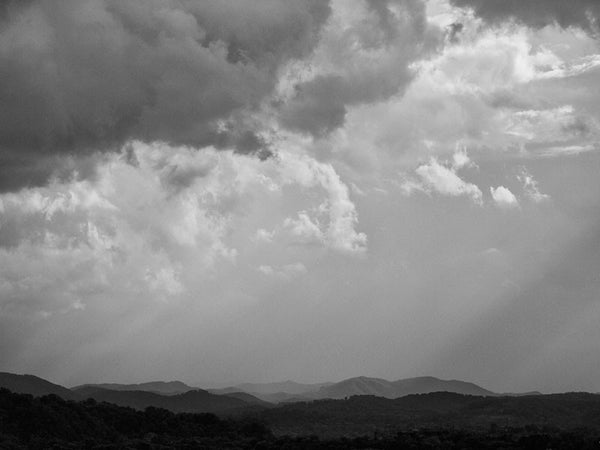 Black and white landscape photograph of storm clouds with sun beams shining through onto the ancient peaks of the Smoky Mountains.