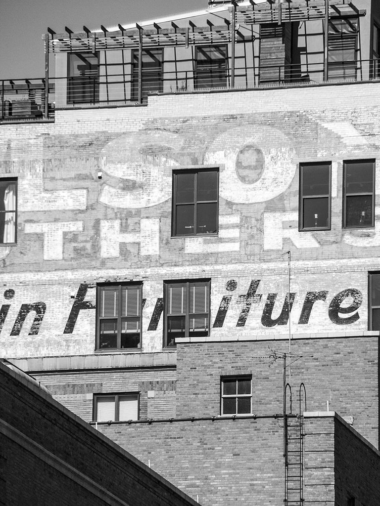 Black and white architectural photograph of buildings in downtown Milwaukee featuring faded vintage advertising signs cut through with modern windows added later