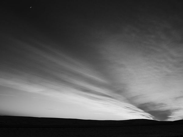 Black and white landscape photograph of the high plains of South Dakota after sunset. Small in the top, left corner can be seen the crescent moon.