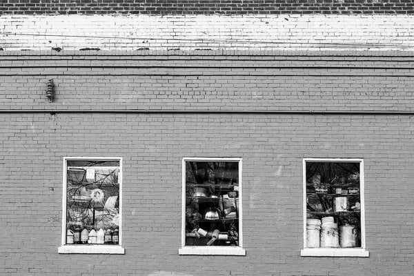 Black and white photograph of three restaurant kitchen windows filled with large cooking pots and other restaurant supplies, seen in East Nashville, Tennessee.