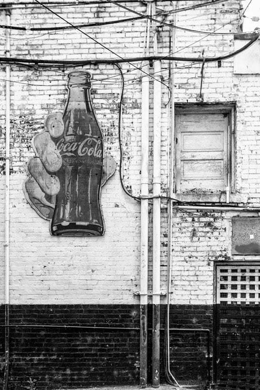 Black and white photograph of a vintage Coca Cola sign in a grimy alley in downtown Nashville, Tennessee. 