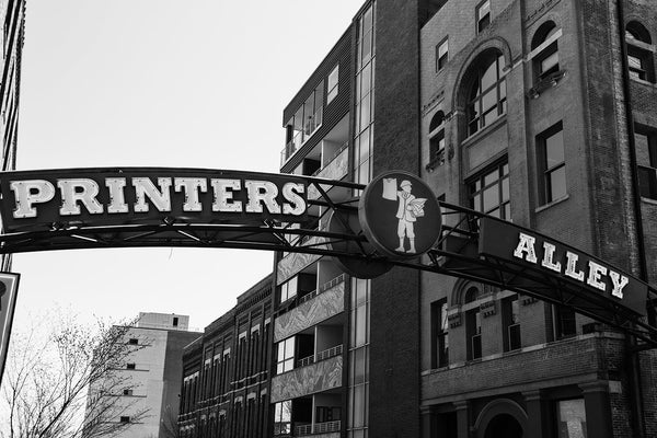 Black and white photograph of the sign that marks the entrance to the famous Printer's Alley entertainment district in Nashville, Tennessee. Originally part of the notorious Nashville men's district of bars and bordellos, the alley transformed into a printing district, with 13 publishers and 10 printers. Nightclubs began entering the area in the 1940s, and the alley remains an entertainment center, even as it again transforms with the entry of modern boutique hotels.