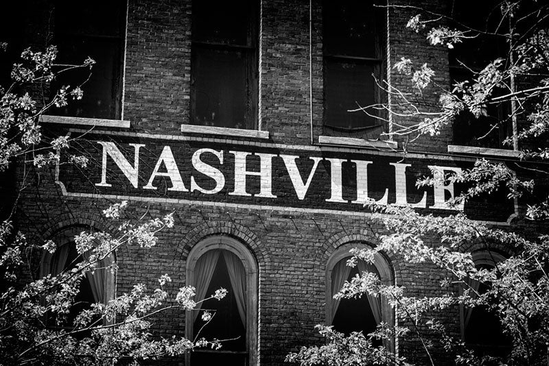 Black and white photograph of a Nashville sign painted on a brick wall facing the Nashville waterfront.