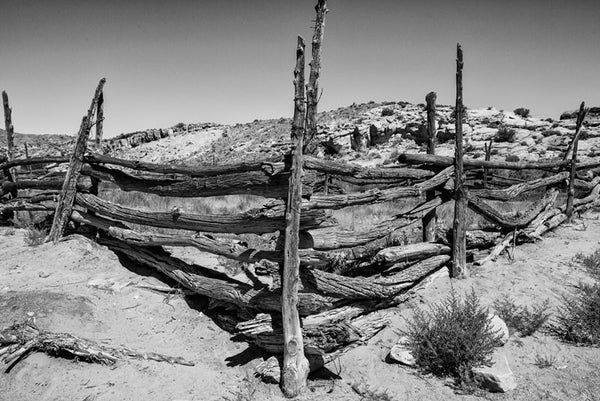 Black and white landscape photograph of an abandoned wooden horse corral in the Utah desert.