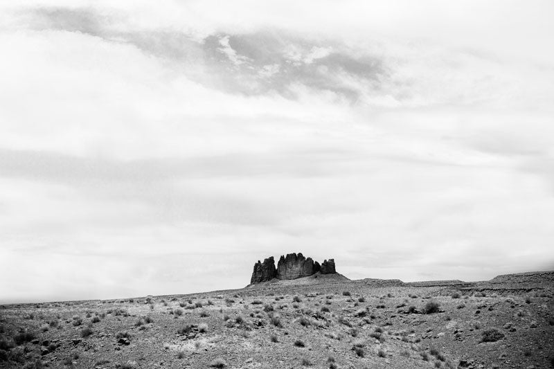 Black and white landscape photograph of red rock cliffs jutting up from the wide, rolling desert floor in Utah.