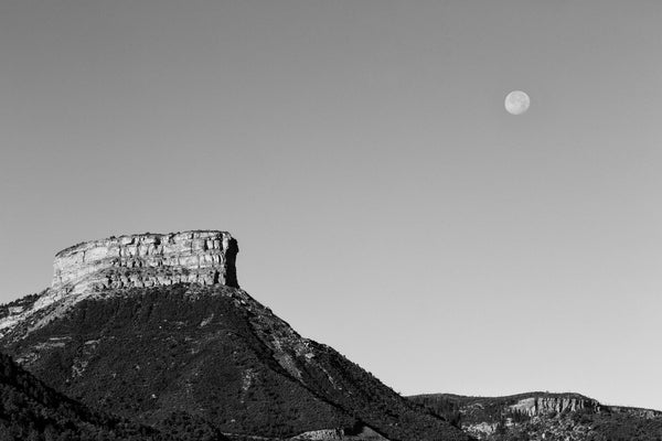 Black and white landscape photograph of the moon in the morning sky above the mountaintop at Mesa Verde, Colorado.