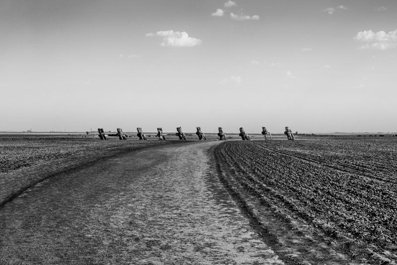 Black and white landscape photograph of the flat Texas landscape around the famous public art piece "Cadillac Ranch," in Amarillo, Texas.