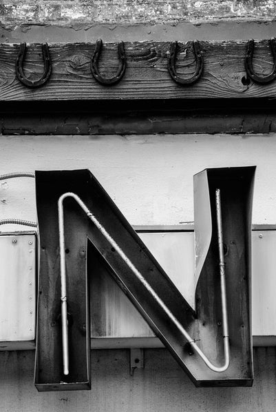 Black and white photograph of a dented red neon letter N with a row of lucky horseshoes nailed above it, spotted on Lower Broadway in Nashville, Tennessee.