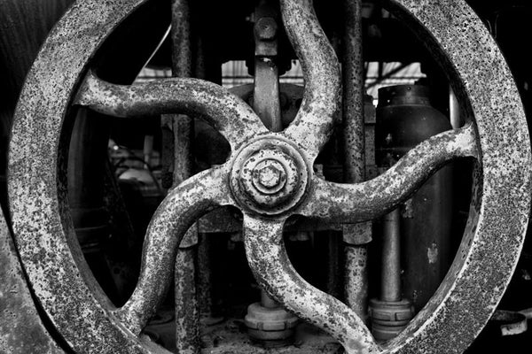 Black and white photograph of a rusty wheel with spokes resembling a wavy star, on an antique red fire wagon.