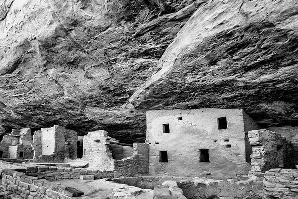 Black and white fine art photograph of Spruce Tree House, seen in its sheltered location under the overhanging edge of Mesa Verde in Colorado.