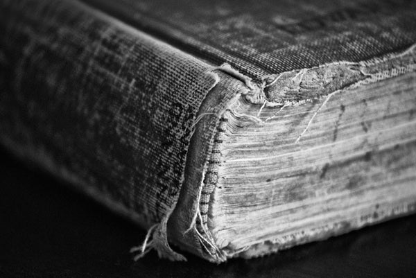 Black and white detail photograph of the worn pages and tattered spine of an old history book from 1904 lying on a black table.