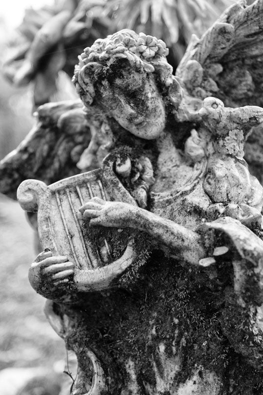 Black and white photograph of a small moss-covered cemetery angel in Savannah's famous, beautiful, and creepy Bonaventure Cemetery.