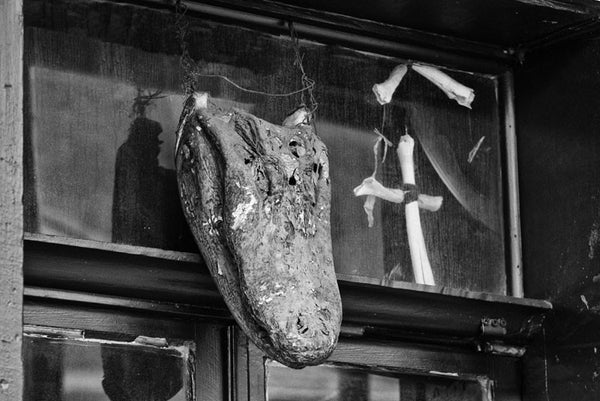 Black and white fine art photograph of an alligator skull and assorted bones -- voodoo talismans over the door to a voodoo museum in New Orleans. 