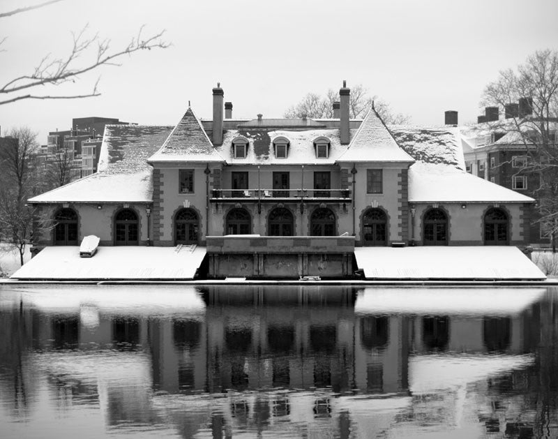 Black and white photograph of Harvard's Weld Boat House in winter, reflecting in the cold, black Charles River.
