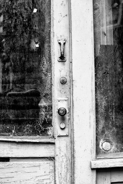 Black and white fine art photograph of a white door with cobwebs in the windows for an abandoned storefront in downtown Memphis, Tennessee.