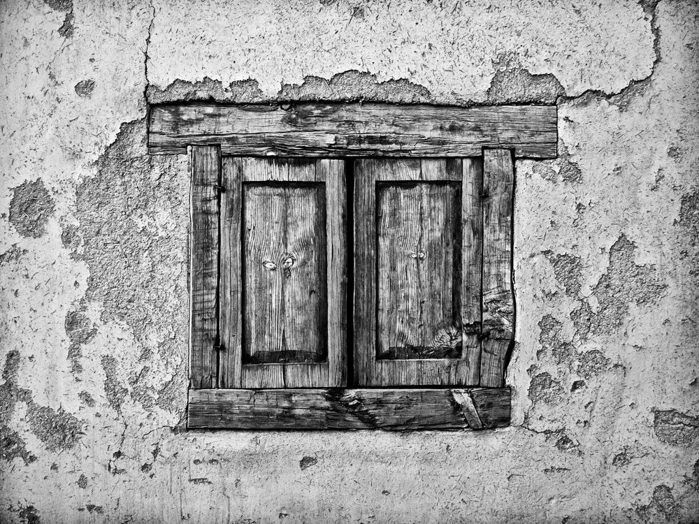 Black and white architectural detail  photograph of the textural adobe walls and shuttered window of an old house in Taos, New Mexico, where Kit Carson once lived.