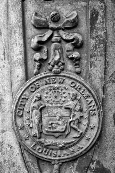 Black and white photograph of an ornate "City of New Orleans Louisiana" street pole crest, seen along Basin Street in New Orleans. 