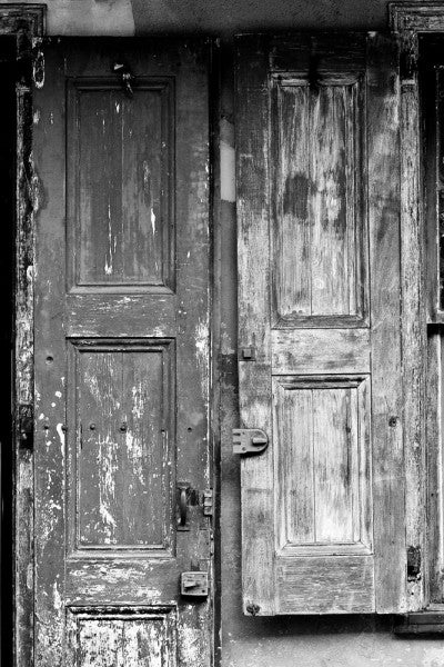 Black and white photograph of a weathered French-style wooden door and window shutter in the French Quarter of New Orleans.