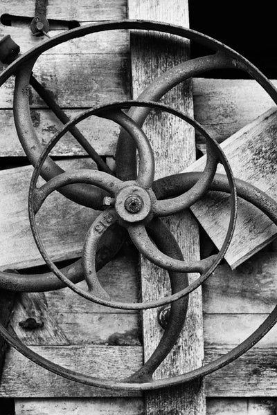 Black and white photograph of a piece of antique farm equipment featuring wheels inside of wheels.