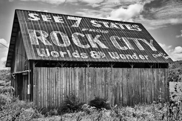 Black and white photograph of a rural barn featuring the famous and historic See Rock City ad painted on its tin roof. 